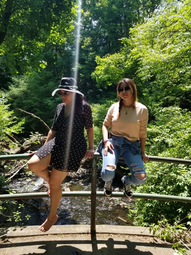 Two brunettes sit on a bridge railing, backlit by the noon sun.