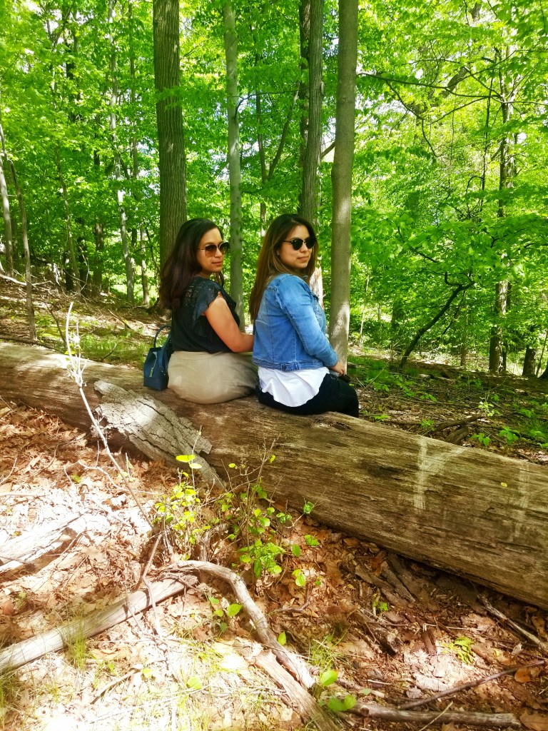 Two brunettes sit on fallen tree trunk, looking over their shoulders at the camera.