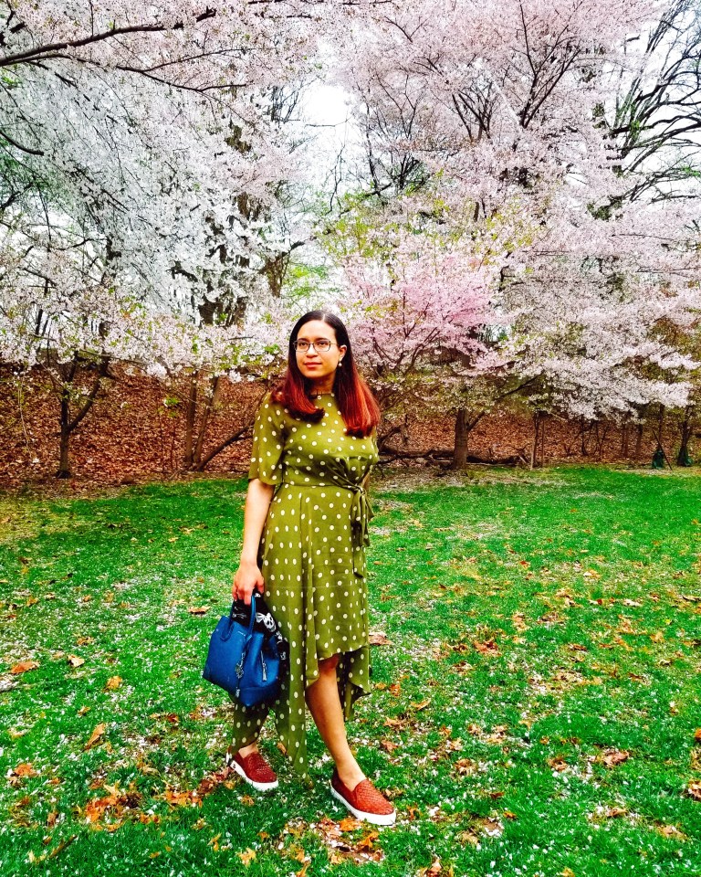 Brunette poses with teal handbag in cherry blossom grove.