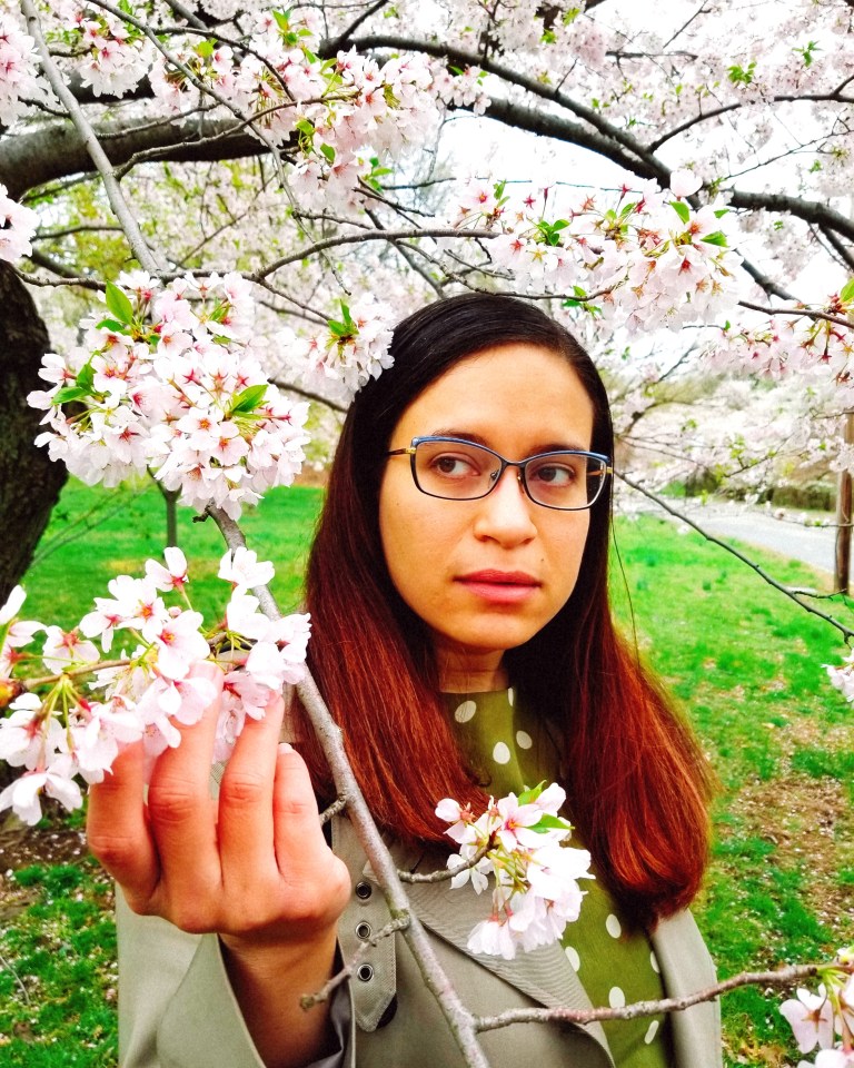 Brunette cradles a frond of cherry blossoms.
