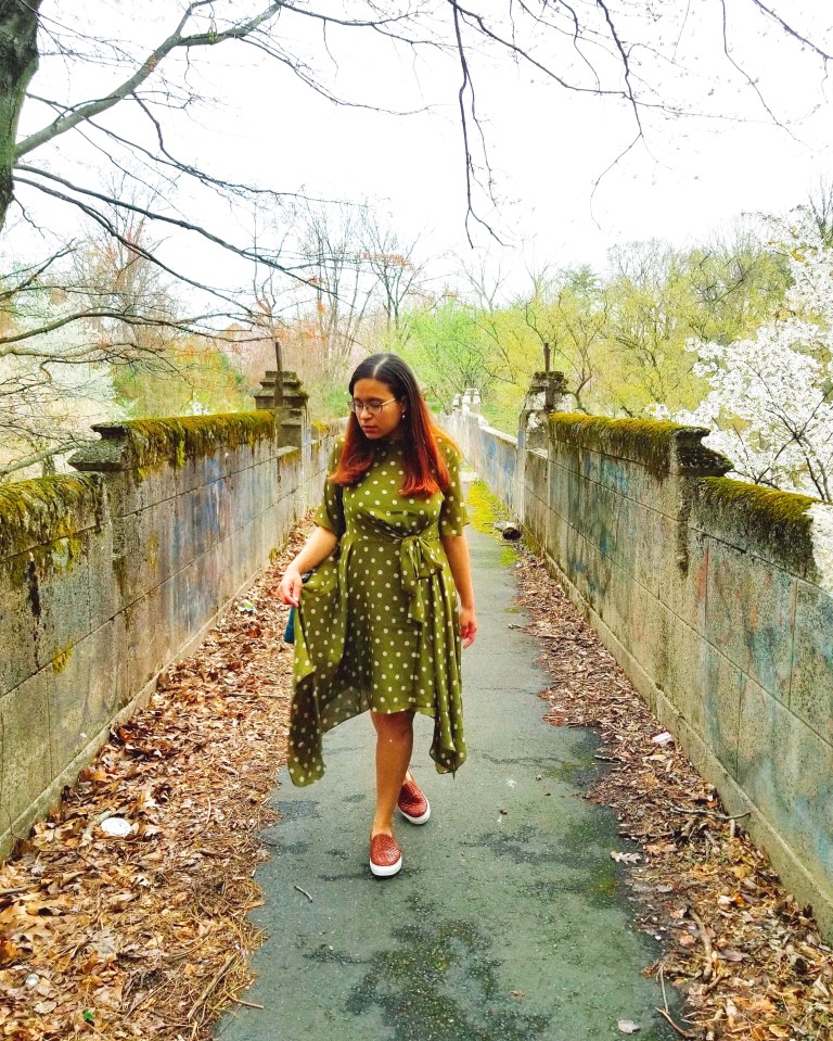 Brunette poses in olive green dress on decrepit bridge.