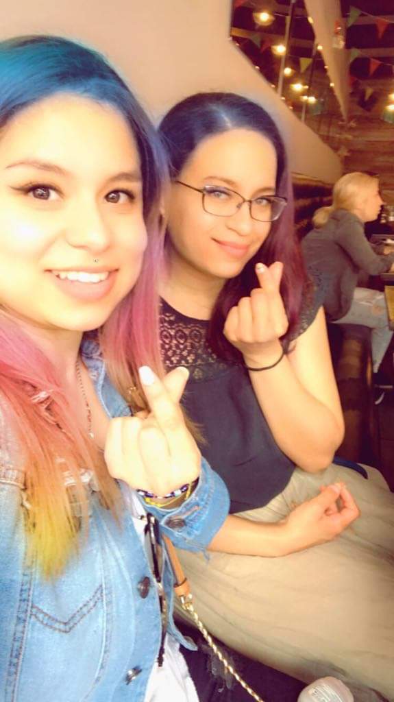 Two brunettes smile and make hearts with fingers; filter turns their hair rainbow.