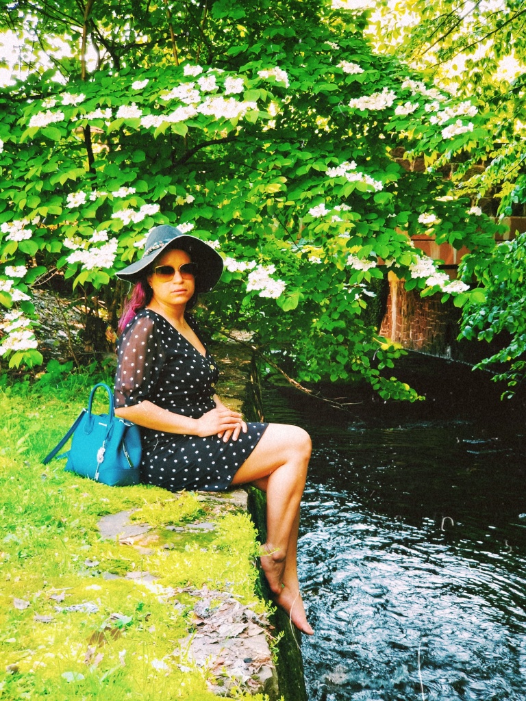 Brunette sits at the edge of a walled stream, teal handbag set down behind her.